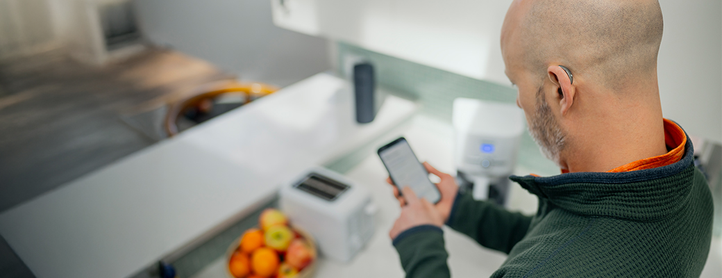 Image of male hearing aid wearer using the My Starkey app in his kitchen